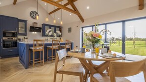 A modern kitchen with blue cabinets, a wooden dining table, and a large window offering a view of a green landscape.