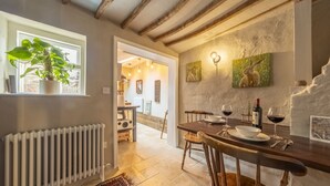 Un comedor rústico con una mesa de madera dispuesta para dos personas, un radiador y una planta en maceta junto a la ventana.