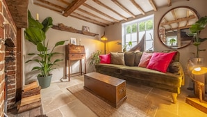 Una sala rústica con vigas de madera a la vista, un sofá verde con cojines rojos, un cofre de madera y un espejo grande.