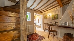 Una escalera de madera que conduce a un comedor con decoración rústica, que incluye un tapiz estampado y sillas de madera.
