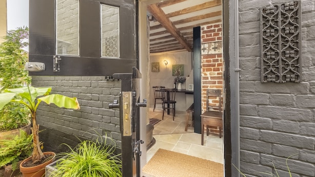 Una puerta negra con un panel de vidrio texturizado, una planta en maceta y un muro de ladrillo con una placa de metal decorativa.