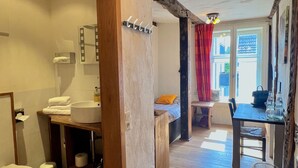A bathroom with a wooden vanity, a toilet, and a sink. There is a mirror above the sink and a towel rack. The bathroom leads to a dining area with a table and chairs. - Hotel Pemü (Arnsberg)
