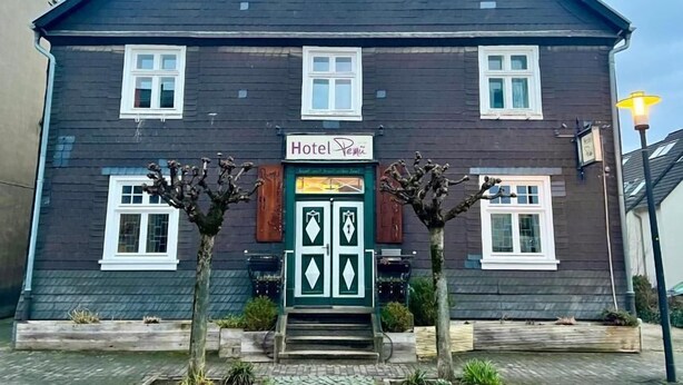 A two-story building with a dark facade, a green door, and a sign reading "Hotel Penzin". - Hotel Pemü (Arnsberg)