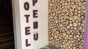 A hotel interior with a wall displaying the word "HOTEL" in large letters, a wooden log wall, and two grey cushioned benches. - Hotel Pemü (Arnsberg)