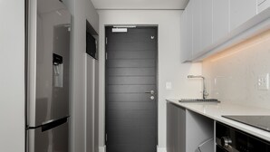 Een kleine keuken met een moderne zwarte deur, roestvrijstalen apparatuur en een marmeren aanrecht.