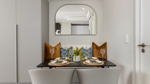 Een eetgedeelte met een zwarte tafel, twee grijze stoelen, een witte vaas met een plant en een spiegel aan de muur.