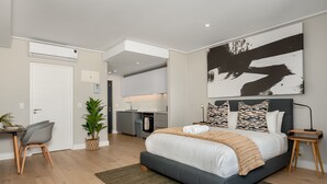 Een moderne slaapkamer met een groot bed, een bureau en een kitchenette op de achtergrond.