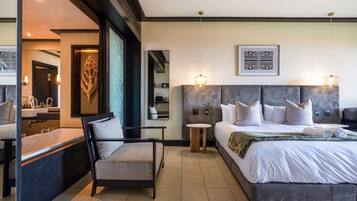 Une chambre d’hôtel moderne dotée d’un grand lit, d’un coin salon avec un fauteuil, d’une petite table ronde et d’une salle de bain avec une baignoire et un lavabo.