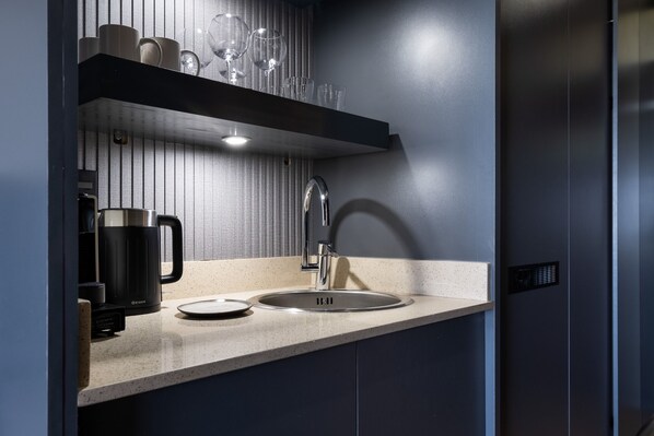 Una cucina moderna con lavello in acciaio inossidabile, una macchina per il caffè e un ripiano in vetro sopra il bancone.