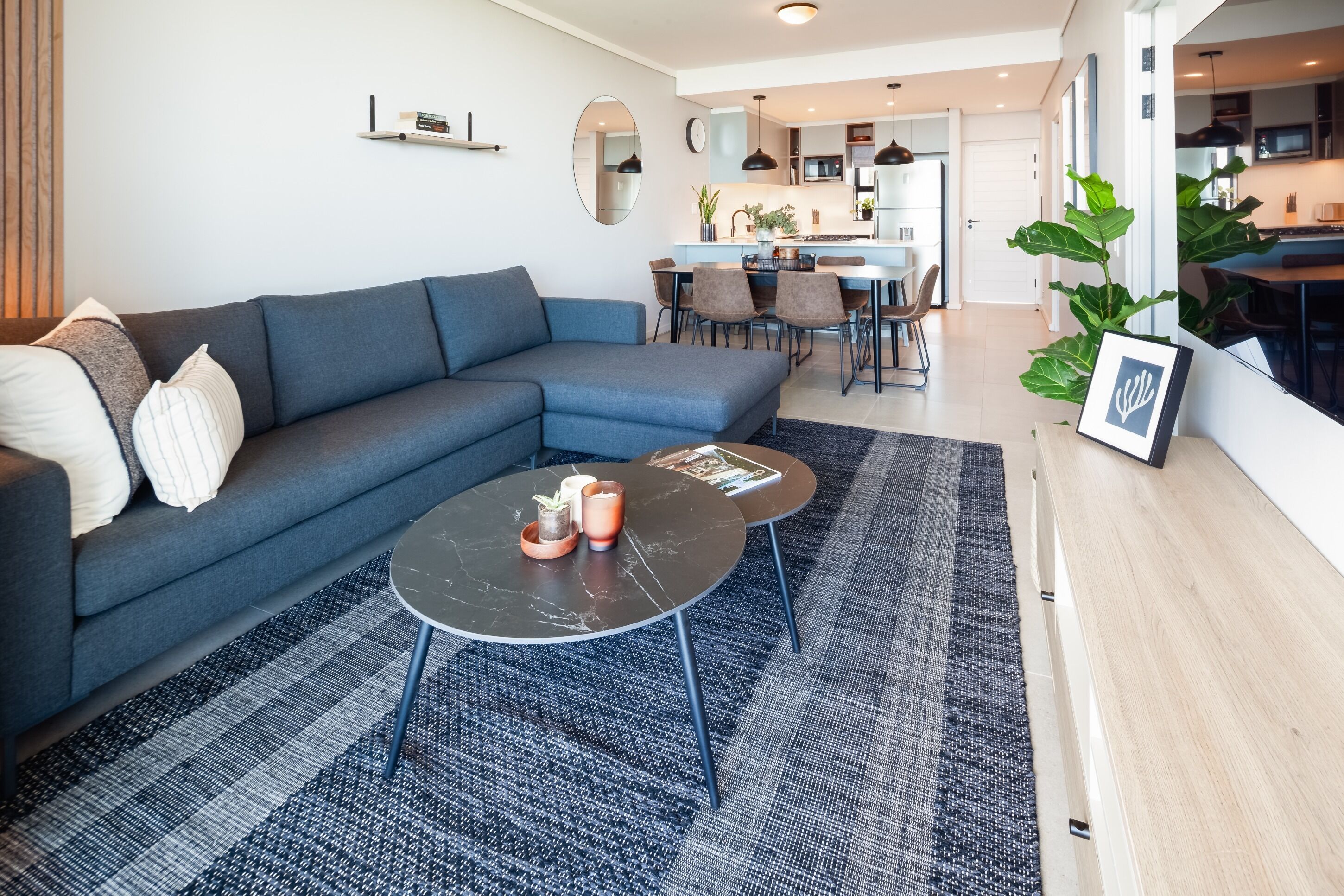Un salon moderne avec un canapé d’angle, une table basse ronde et un coin repas avec des chaises.