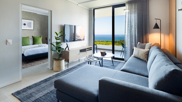 A modern hotel room with a balcony, a sofa, a small table, and a bed with green pillows. - Stunning Sea Views , Inverter , Steam Room (Umhlanga)