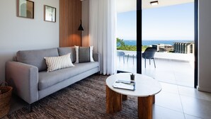 Un salon moderne avec un canapé gris, une table basse ronde et une vue sur la mer grâce à une grande porte-fenêtre coulissante.