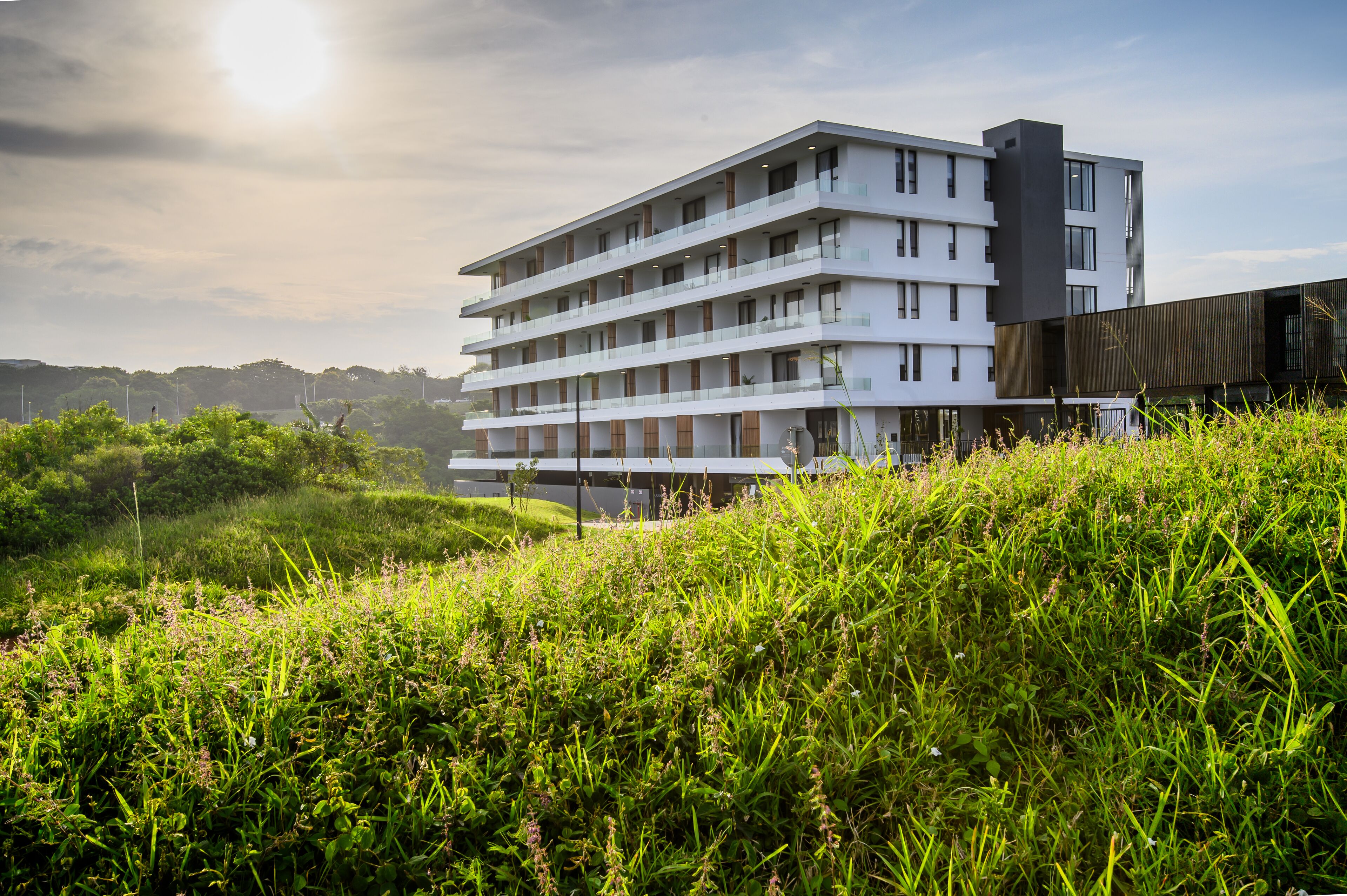 Un hotel de varios pisos con un diseño moderno, que cuenta con balcones en cada planta y un techo plano.