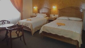 Habitación de hotel con dos camas individuales, cabecera de madera, una mesita y una silla.