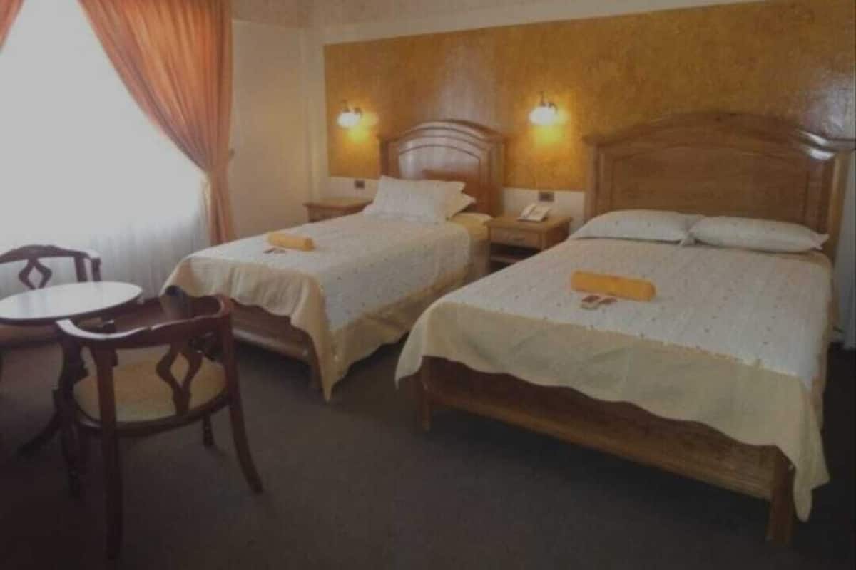 A hotel room with two single beds, a wooden headboard, a small table, and a chair.