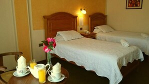 Habitación de hotel con dos camas, una mesita de noche con lámpara, un teléfono y un cuadro en la pared.