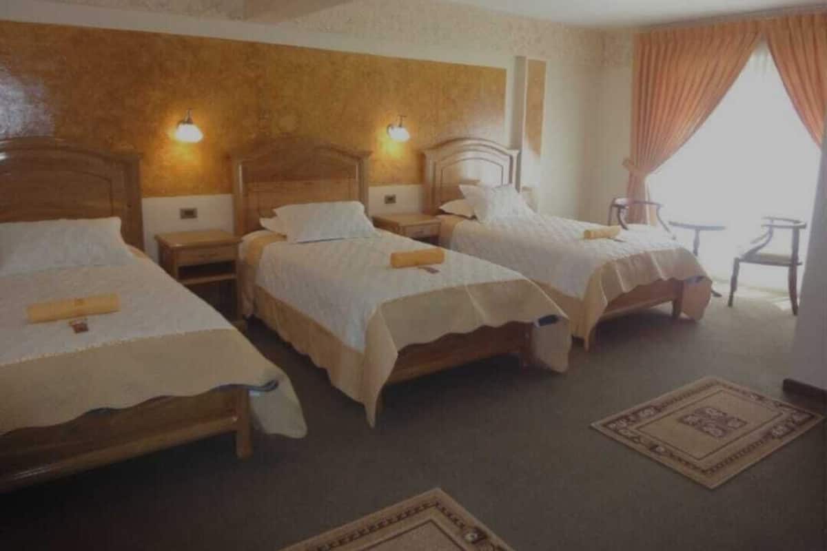 A hotel room with two single beds, a small table, and a chair.