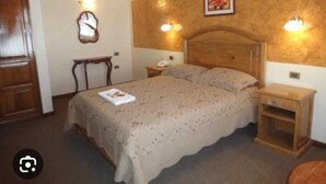 Un dormitorio con una cama de madera, mesitas de noche, un velador, un espejo e iluminación en la pared.