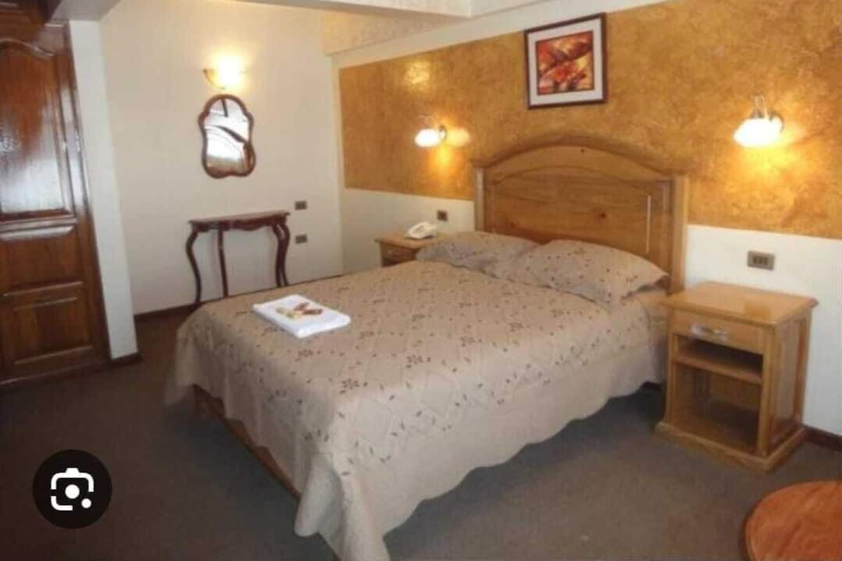 A bedroom with a wooden bed, bedside tables, a nightstand, a mirror, and wall-mounted lights.