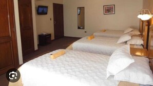 Habitación de hotel con tres camas, un televisor, un espejo y un cuadro en la pared.