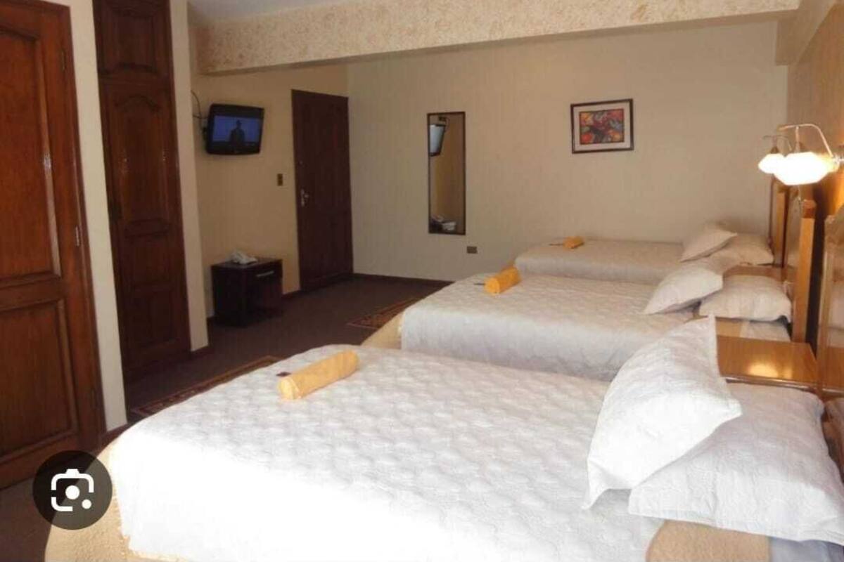 A hotel room with three beds, a television, a mirror, and a painting on the wall.