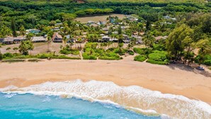 Ein Luftbild einer Küstenregion mit einem Sandstrand, einer kleinen Siedlung mit Häusern und Palmen sowie freiem Blick auf den Ozean.