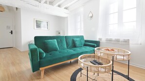 Una sala de estar moderna con un sofá verde azulado, dos mesitas de mimbre y piso de madera.