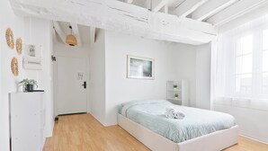 Un dormitorio con una cama, un armario blanco, una planta pequeña y una ventana con cortinas.
