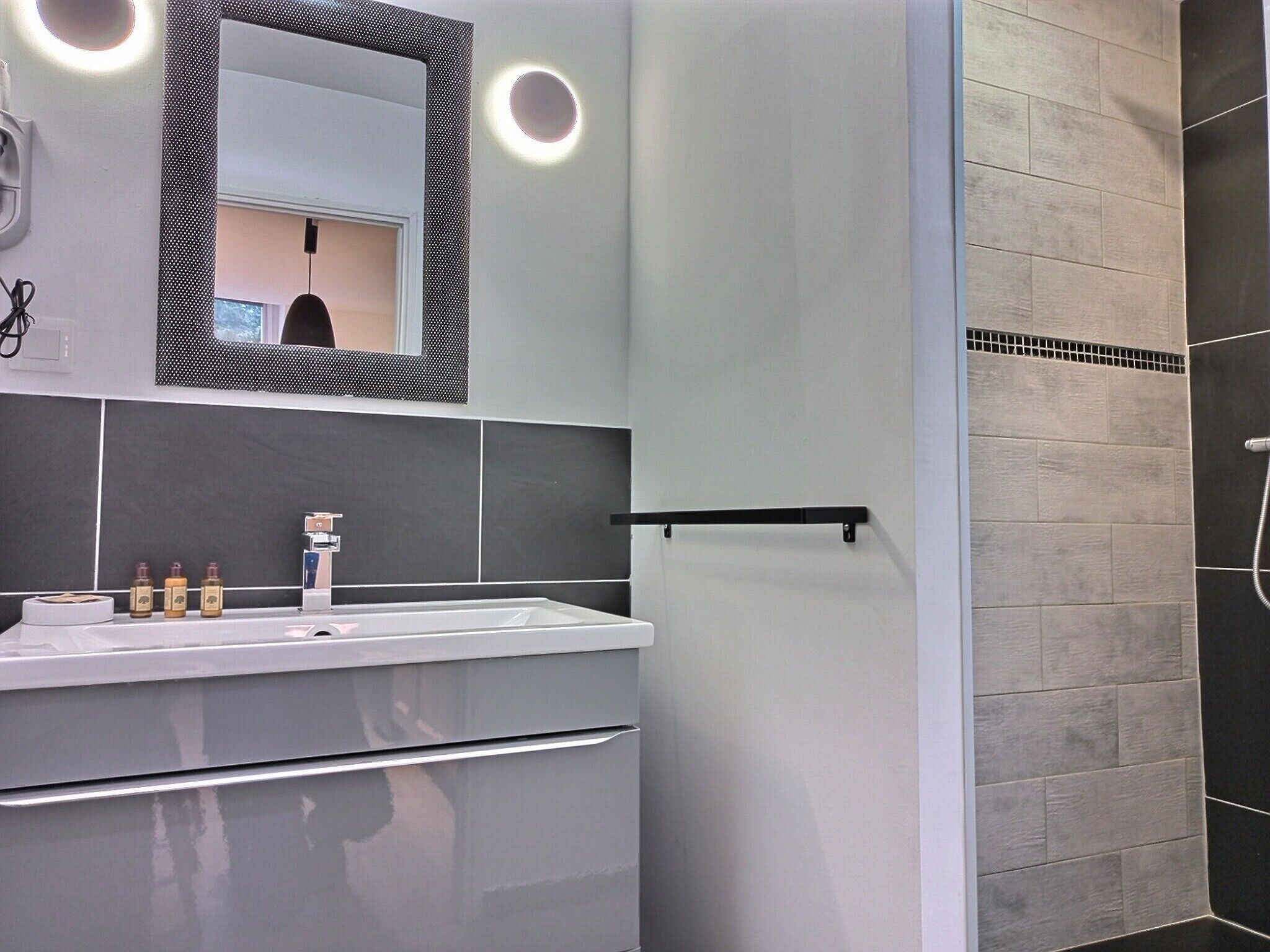 Un bagno moderno con un lavandino bianco, piastrelle scure e una zona doccia.