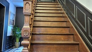 Eine Holztreppe mit aufwendiger Balustrade und Handlauf, die zu einem Zwischenpodest mit Schachbrettmuster führt.