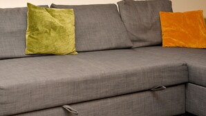 En grå hjørnesofa med pude og hynde, begge i grå farve.