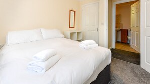 Et hotelværelse med en stor seng, et natbord, et spejl og en dør til et badeværelse.