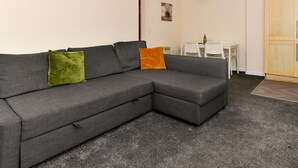 En grå modulsofa med to puder, et hvidt spisebord med stole og en træskab i en stue.