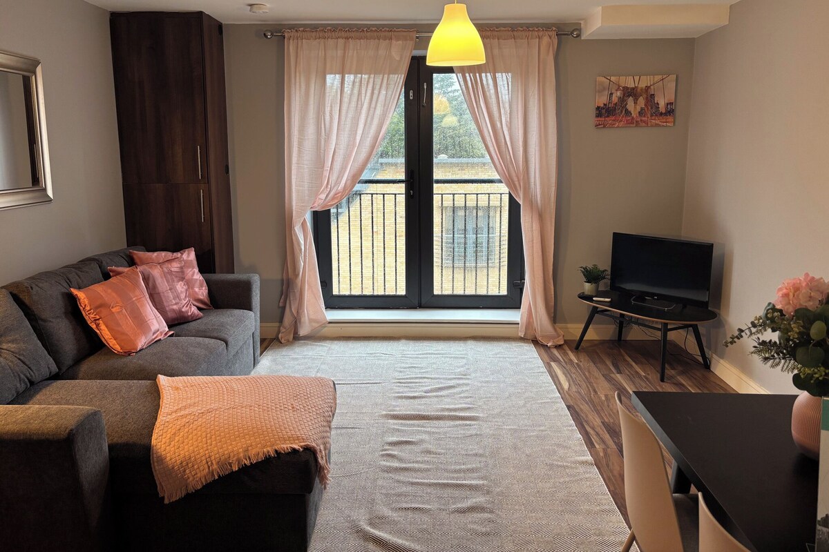 A living room with a sofa, a TV, a dining table, and a large window with curtains.