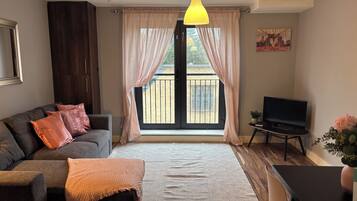 A living room with a sofa, a TV, a dining table, and a large window with curtains.