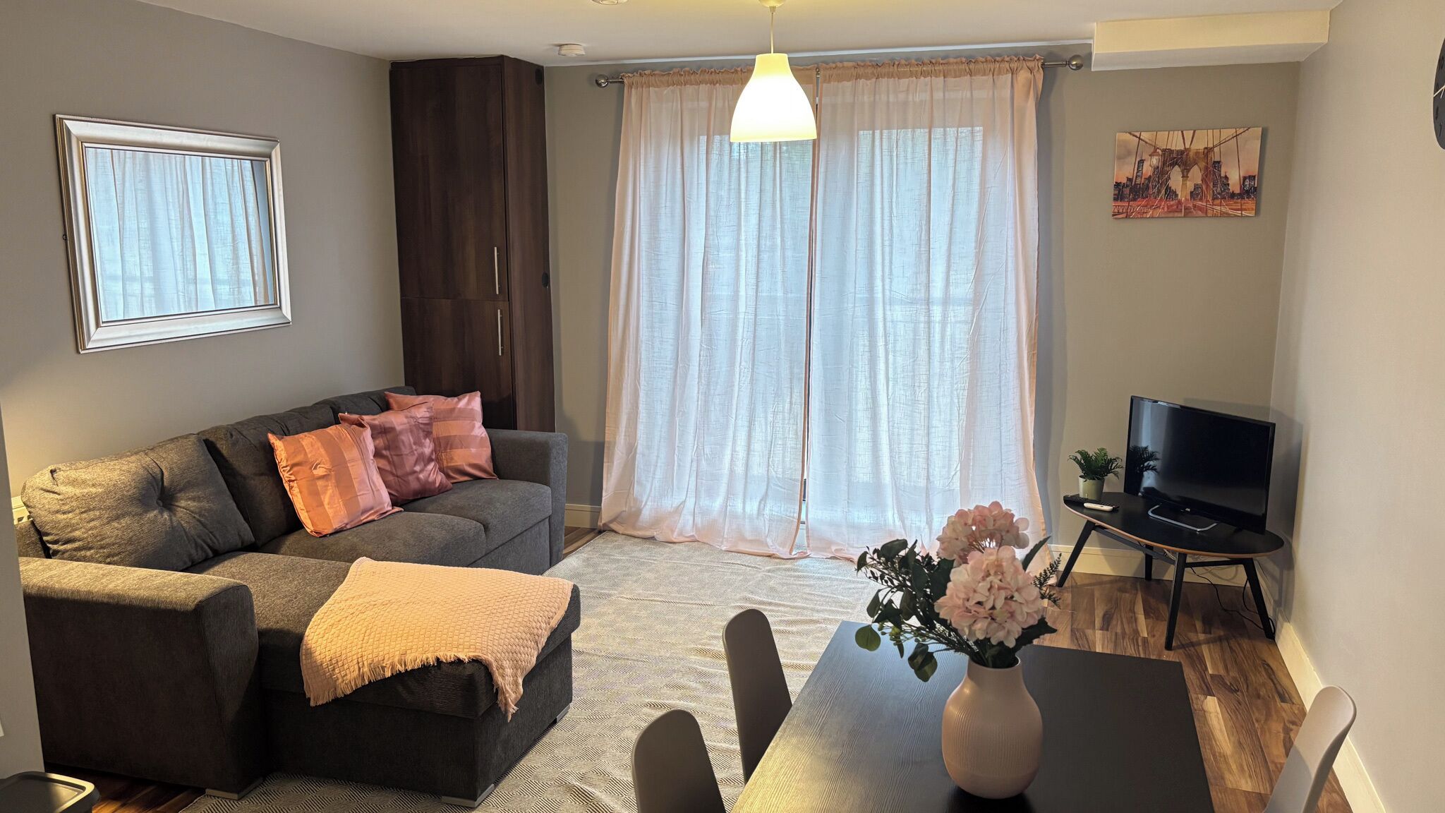 A living room with a sofa, a TV, a dining table with chairs, and a window with curtains.