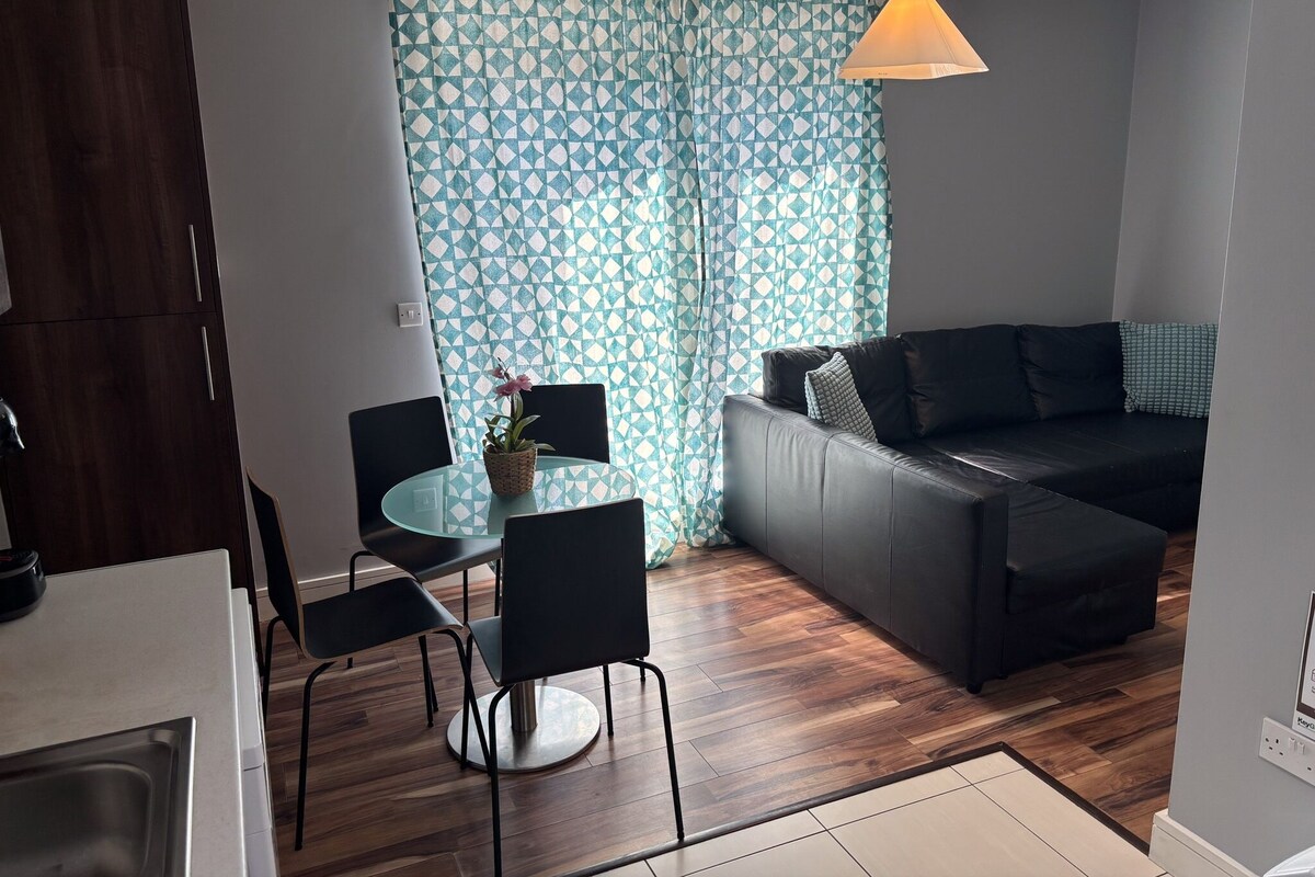 A modern living space with a dining area, a sofa, and a kitchen.