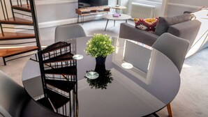 Una sala de estar moderna con una mesa redonda de vidrio, un sofá, un televisor y una escalera.