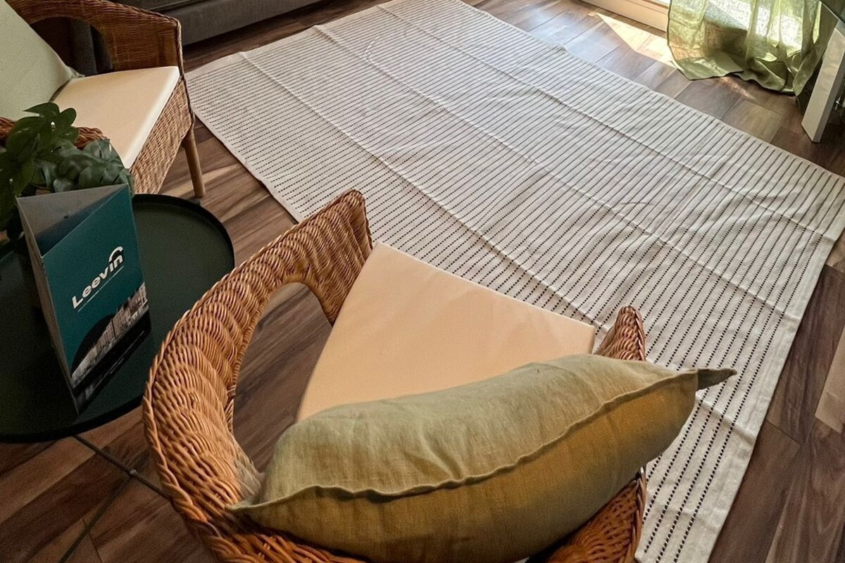 Un salon avec un canapé, un fauteuil en osier, une grande moquette et des œuvres d’art accrochées au mur.