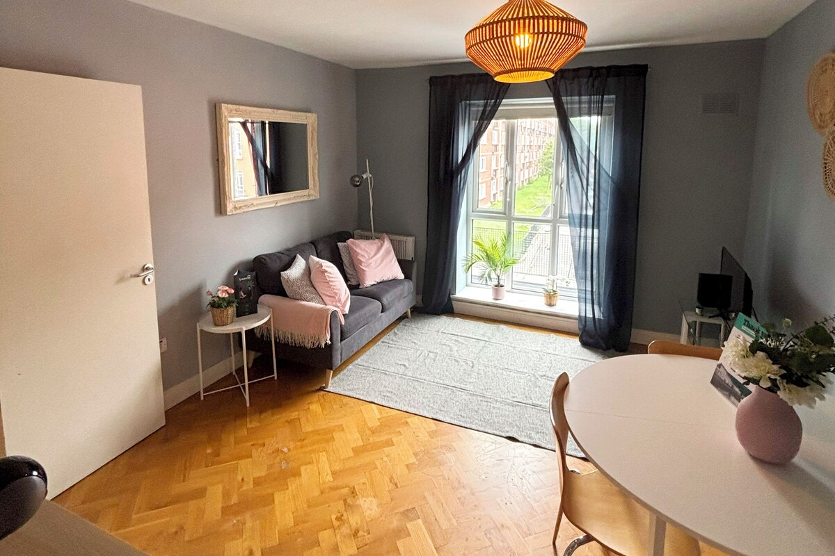 A room with a sofa, a dining table, a hanging light fixture, and a window with a view.