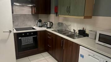 A compact kitchen with a dishwasher, oven, microwave, and a hanging light fixture.