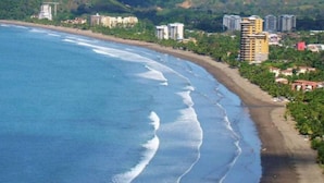Eine Küstenlandschaft mit Strand, Gebäuden und Hügeln im Hintergrund.