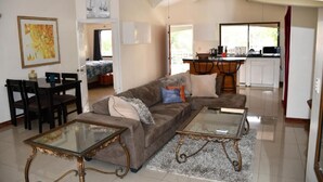 Ein Wohnzimmer mit einer Couch, zwei Couchtischen mit Glastischplatten und einem Essbereich mit Stühlen.
