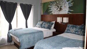 A hotel room with two beds, a large floral artwork on the wall, and a ceiling air conditioner. - 11B Jaco Sol Quadplex - Luxury apartment near the beach and commerce (Jacó)