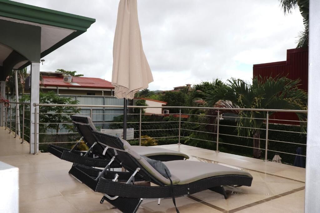 A balcony with two reclining chairs and a large umbrella, overlooking a residential area with houses and greenery.