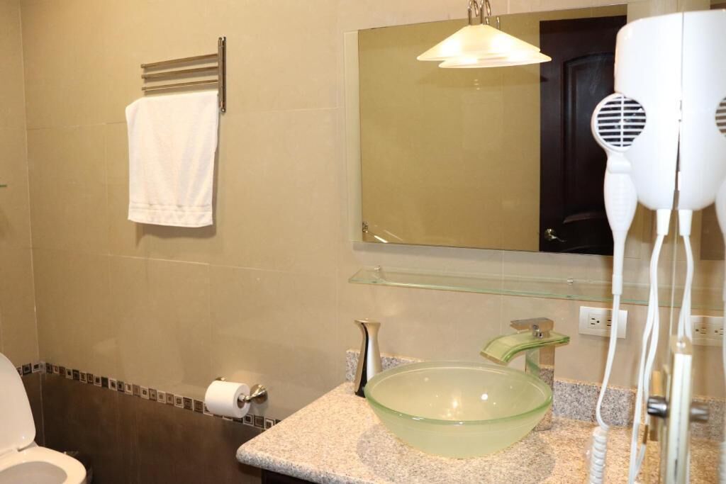 Een badkamer met een wastafel van glas, een handdoekrek met een witte handdoek, een spiegel en een haardroger.