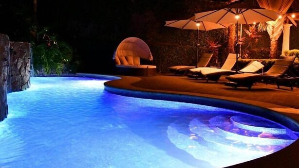 A swimming pool with a curved edge, surrounded by lounge chairs and umbrellas. - 11B Jaco Sol Quadplex - Luxury apartment near the beach and commerce (Jacó)