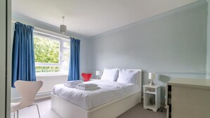 Een moderne slaapkamer met een groot bed, witte wanden en blauwe gordijnen.