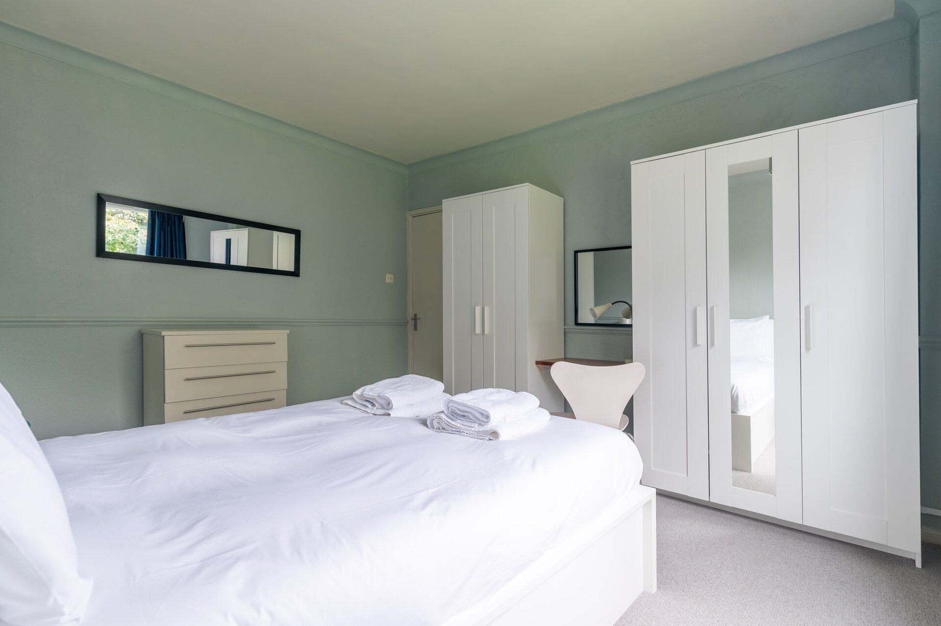 Ein Schlafzimmer mit Bett, Kommode, Kleiderschrank und Spiegel.
