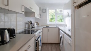 Een moderne keuken met witte kasten, een fornuis, een spoelbak en een raam met uitzicht op groen.